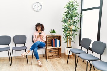 Young middle east woman listening to music sitting on chair at waiting room