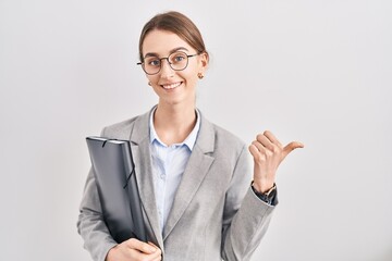 Young caucasian woman wearing business clothes and glasses pointing to the back behind with hand and thumbs up, smiling confident