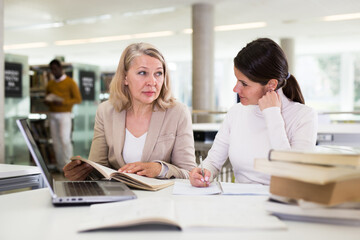 Obraz premium Female teacher working with girl student in university library. High quality photo