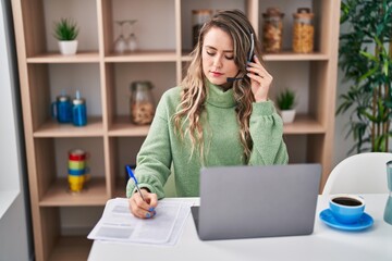 Young woman call center agent writing on document at home
