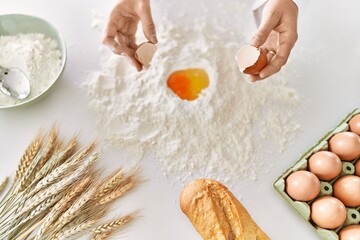 Young woman wearing cook uniform cracking egg on flour at kitchen