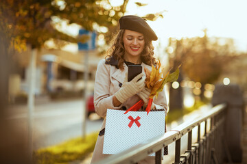 woman with shopping bags and autumn leaves using phone app