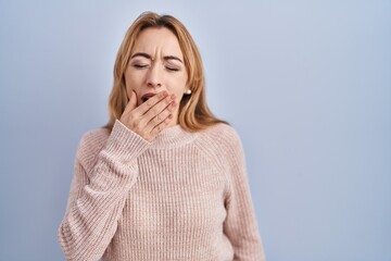 Hispanic woman standing over blue background bored yawning tired covering mouth with hand. restless and sleepiness.