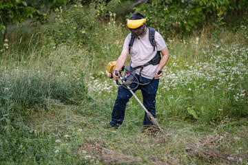 caucasian man farmer using string trimmer to cut grass brush cutter