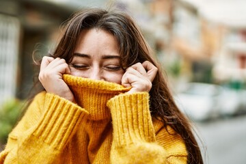 Young beautiful brunette woman wearing turtleneck sweater doing funny gesture covering face with...