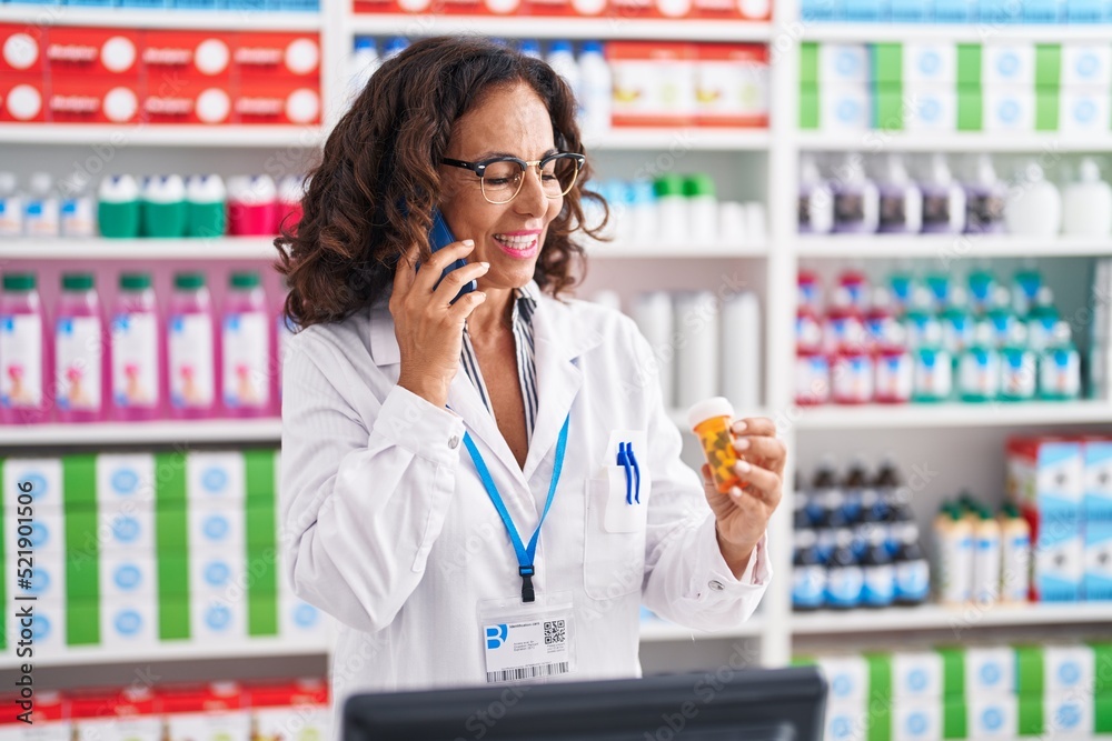 Sticker middle age woman pharmacist holding pills bottle talking on smartphone at pharmacy