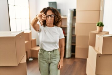 Middle age hispanic woman wearing casual clothes standing around cardboard boxes at new home with...