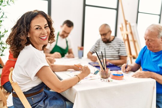 Group of middle age draw students sitting on the table drawing at art studio. Woman smiling happy looking to the camera.