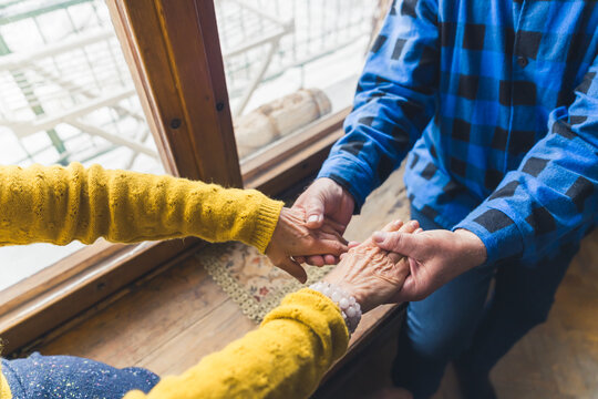 Close up of a married couple of a caucasian old man and a woman holding their hands while sitting near the window. High quality photo