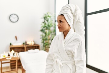 Obraz na płótnie Canvas Young brunette woman wearing towel and bathrobe standing at beauty center looking to side, relax profile pose with natural face with confident smile.