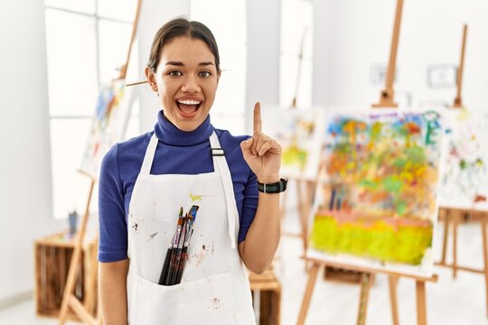 Young brunette woman at art studio pointing finger up with successful idea. exited and happy. number one.