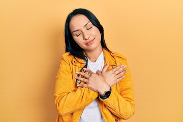 Beautiful hispanic woman with nose piercing wearing yellow leather jacket smiling with hands on chest with closed eyes and grateful gesture on face. health concept.