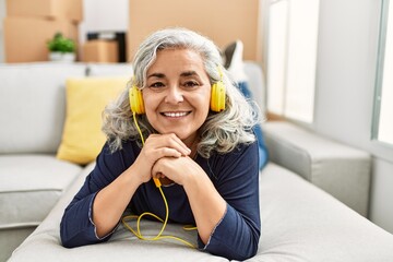 Middle age grey-haired woman listening to music lying on the sofa at new home.