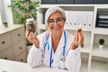 Middle age woman doctor holding cbd oil smiling with a happy and cool smile on face. showing teeth.