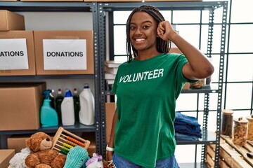 Young african american woman working wearing volunteer t shirt at donations stand smiling pointing...
