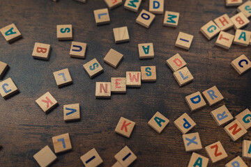 Fototapeta na wymiar Advertisement background idea for news agencies. Colourful square little wooden puzzles creating the word NEWS. Dark-wood table as a background. High quality photo