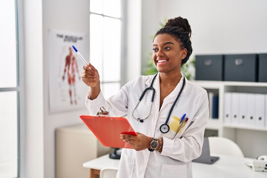 African american woman wearing doctor uniform writing on document at clinic
