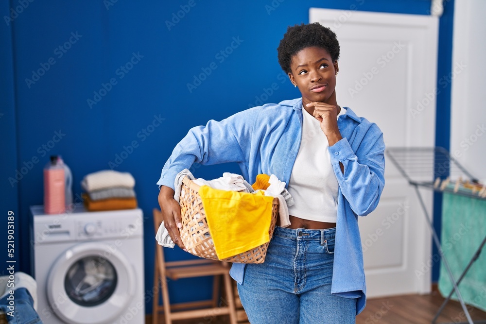 Canvas Prints African american woman holding laundry basket serious face thinking about question with hand on chin, thoughtful about confusing idea