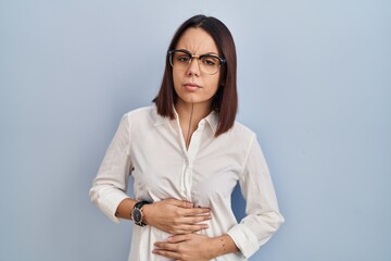Young hispanic woman standing over white background with hand on stomach because indigestion,...