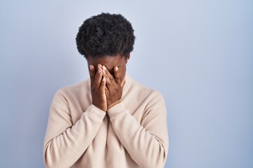 African american woman standing over blue background with sad expression covering face with hands while crying. depression concept.