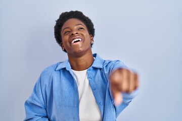 African american woman standing over blue background laughing at you, pointing finger to the camera with hand over body, shame expression