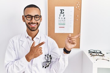 African american optician man standing by eyesight test smiling and looking at the camera pointing...