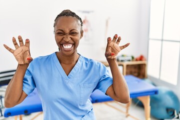 Black woman with braids working at pain recovery clinic smiling funny doing claw gesture as cat,...