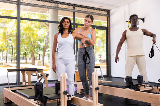 Hispanic woman and african-american man exercising with pilates rings. Young european woman instructor assisting them with workout.