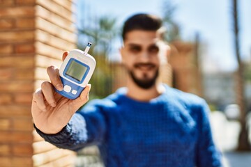 Young arab man smiling confident holding glucometer at street
