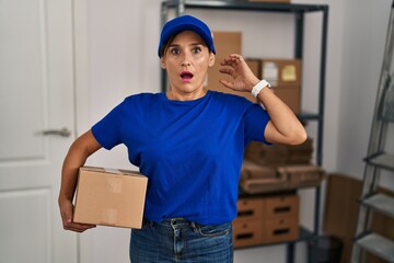 Middle age brunette woman working wearing delivery uniform and cap crazy and scared with hands on head, afraid and surprised of shock with open mouth