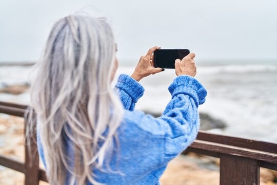 Middle age grey-haired woman make photo by smartphone at seaside