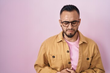 Young hispanic man standing over pink background with hand on stomach because nausea, painful disease feeling unwell. ache concept.