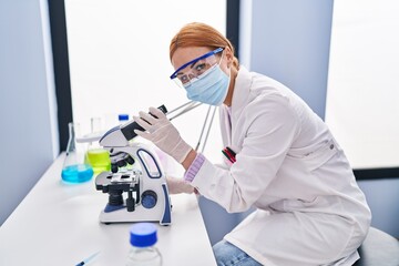 Young caucasian woman scientist wearing medical mask using microscope at laboratory