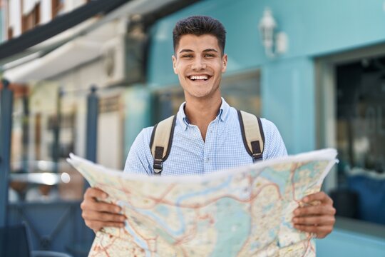 Young hispanic man student smiling confident holding city map at street