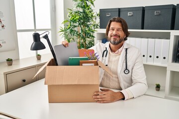 Handsome middle age doctor man holding box with items relaxed with serious expression on face. simple and natural looking at the camera.