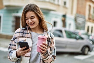 Young blonde woman smiling confident using smartphone holding coffee at street