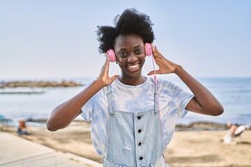 Young african woman listening to music using headphones by the sea