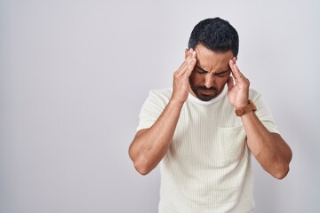 Hispanic man with beard standing over isolated background with hand on head, headache because stress. suffering migraine.
