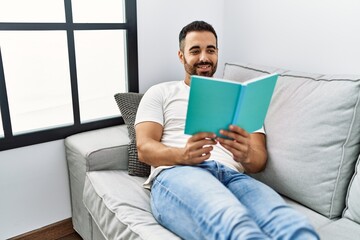 Young hispanic man smiling confident reading book at home