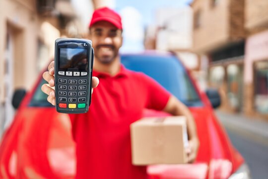 Young hispanic man courier holding package and data phone at street