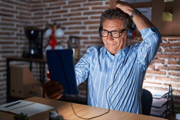 Middle age hispanic man using touchpad sitting on the table at night confuse and wondering about...