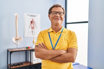 Middle age man physiotherapist smiling confident standing with arms crossed gesture at physiotherpy...