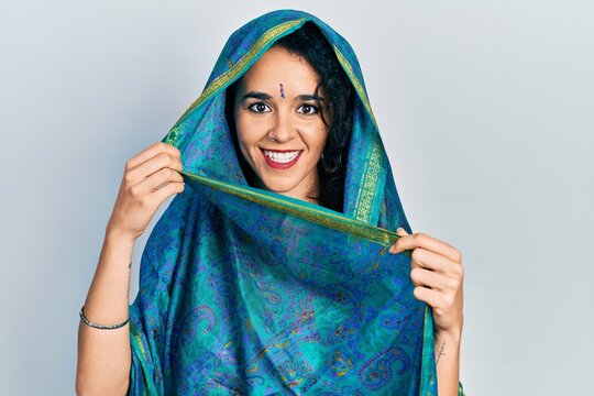Young woman wearing bindi wearing traditional indian saree pointing thumb up to the side smiling happy with open mouth