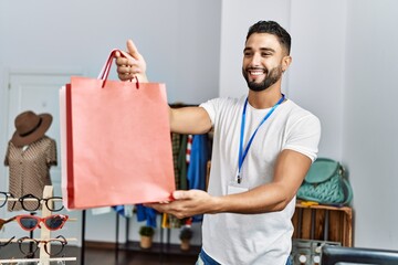 Young arab man shopkeeper holding shopping bags working at clothing store