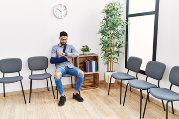 Young arab man sitting on chair with arm sling at clinic waiting room