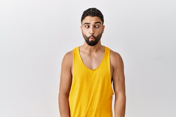 Young handsome man with beard standing over isolated background making fish face with lips, crazy and comical gesture. funny expression.