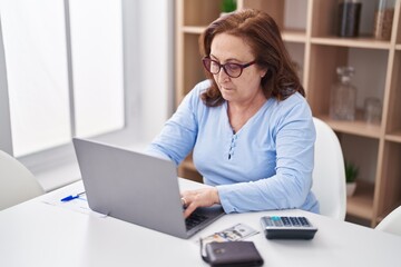 Senior woman using laptop and calculator at home