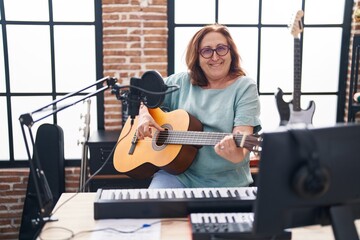 Fototapeta na wymiar Senior woman musician smiling confident playing classical guitar at music studio
