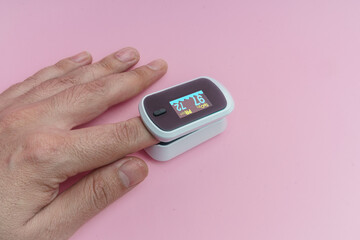 Mano, medición con oximetro y pulsometro sobre fondo rosa.