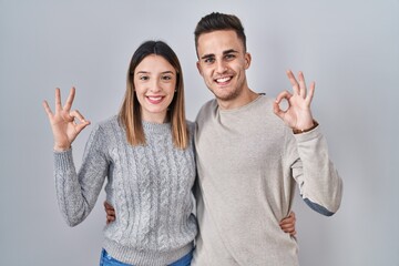 Young hispanic couple standing over white background smiling positive doing ok sign with hand and fingers. successful expression.